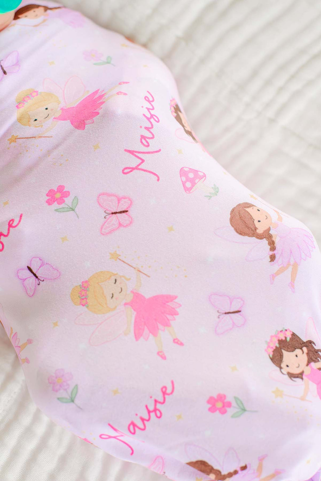 Close-up of the Fairy Wishes personalized swaddle print: pink fairies, butterflies, flowers and a custom name on light pink fabric