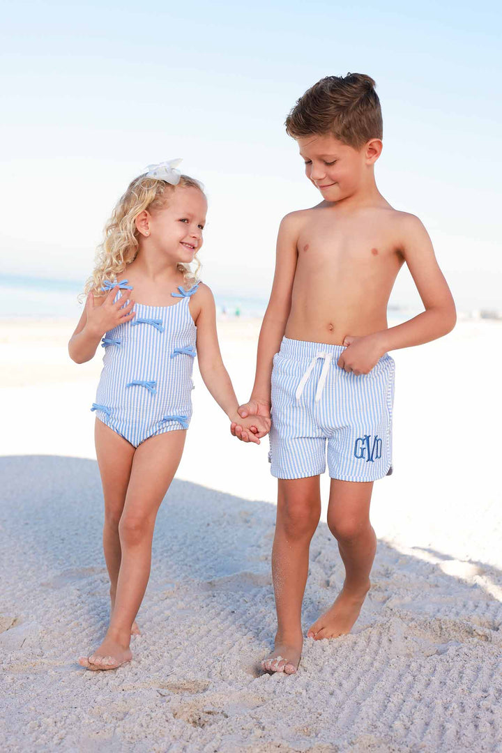 brother and sister holding hands walking on the beach in seersucker matching swimsuits 