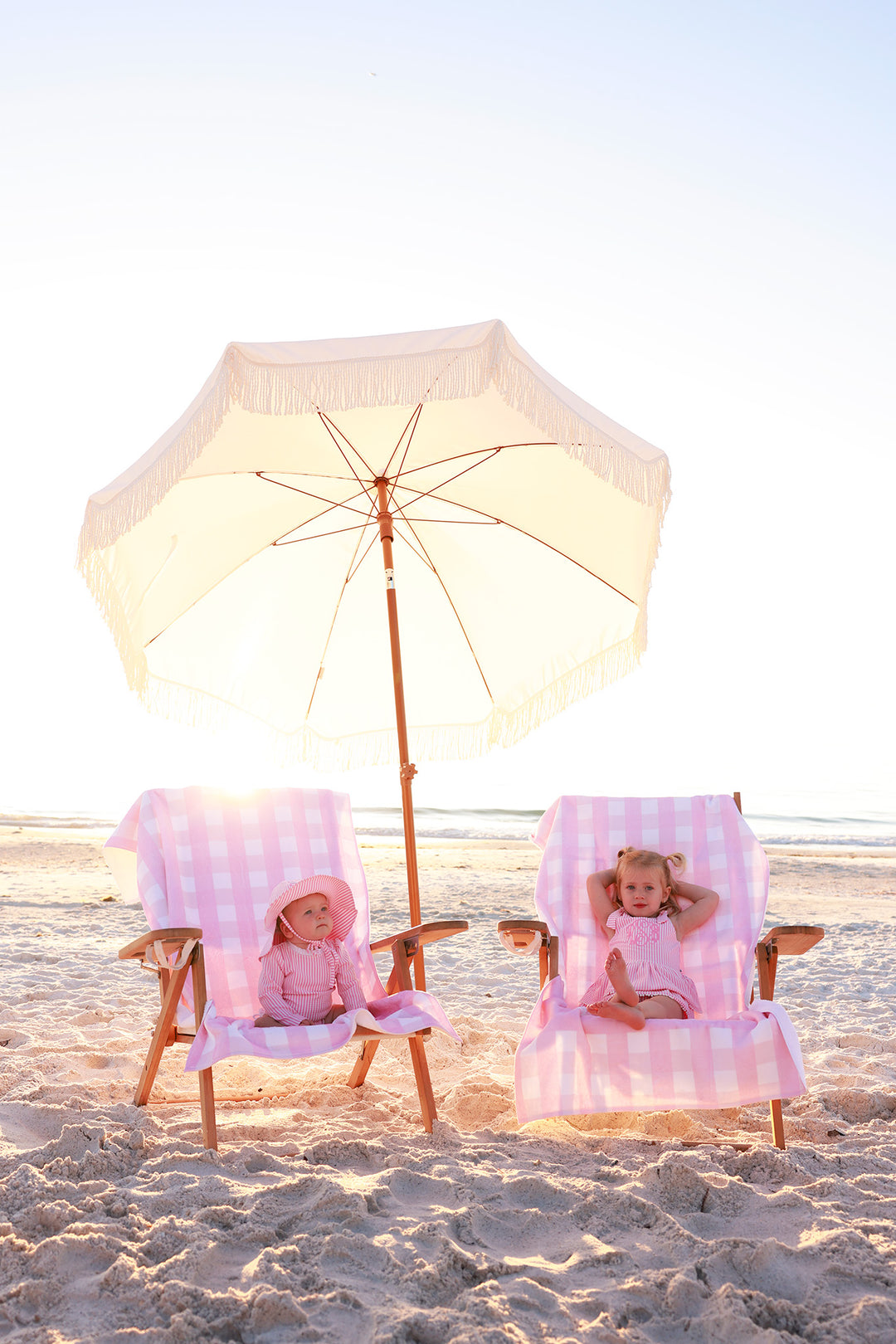 girls sitting on beach chairs with pink seersucker personalized towels and matching seersucker swimsuits 
