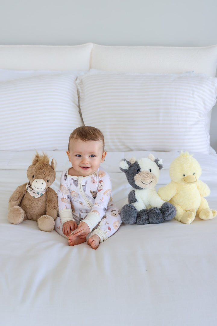 baby boy sitting on bed with horse, cow and duck stuffed animals 