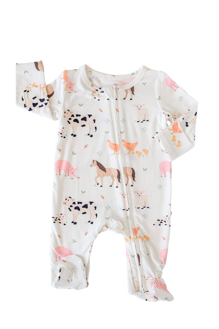 A Caden Lane baby footed sleeper with a front zipper, featuring an all-over farm animal print on a white background. The print includes pink pigs, black-and-white cows, brown horses, chickens, and carrots.