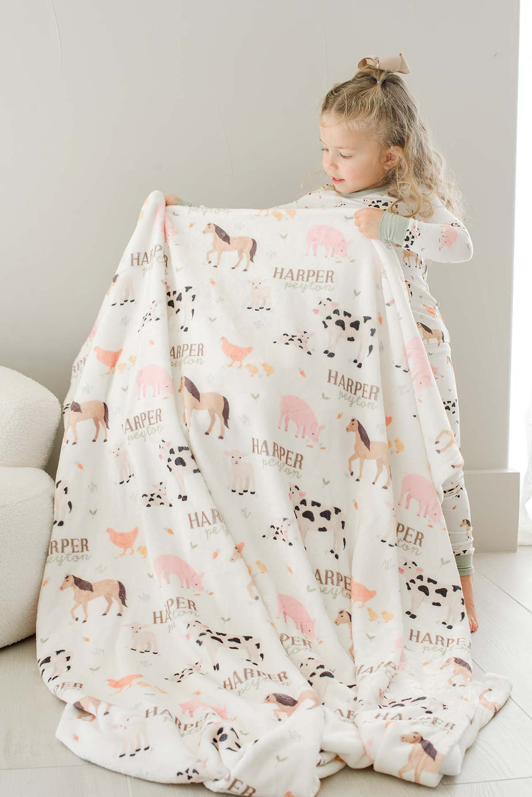 Toddler girl in Caden Lane farm animal pajamas holding up a personalized 'Harper Peyton' farm animal minky blanke