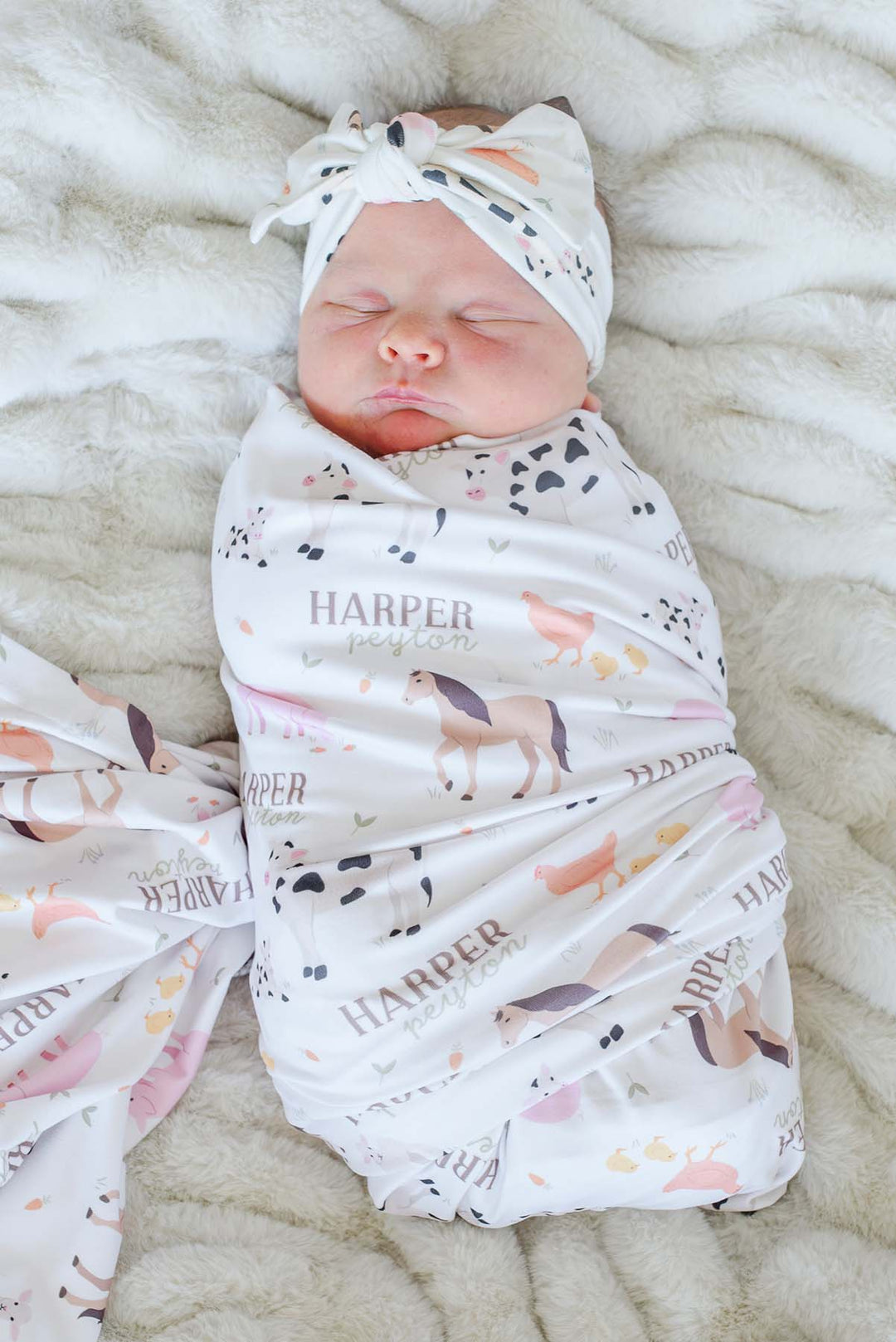 Caden Lane personalized farm animal swaddle blanket with custom name 'Harper Peyton,' shown wrapped around a sleeping newborn with matching knotted headband