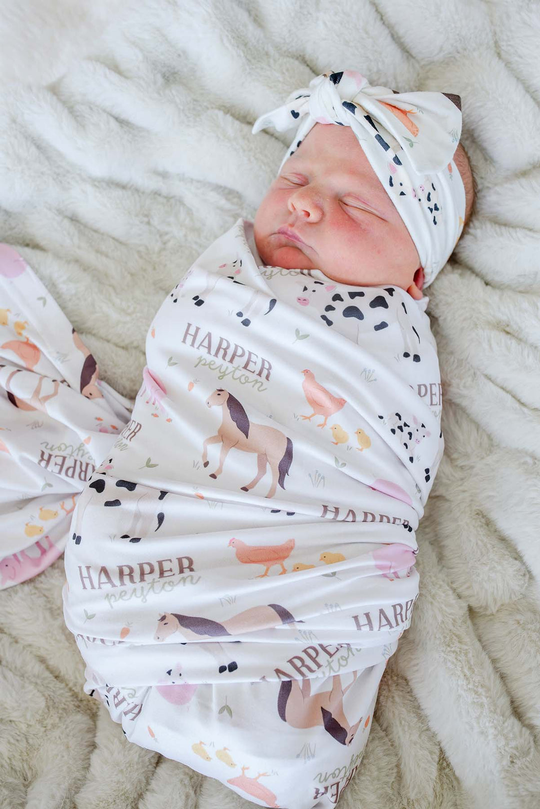 Close-up of sleeping newborn in Caden Lane personalized farm animal swaddle blanket with custom name 'Harper Peyton' and matching headband