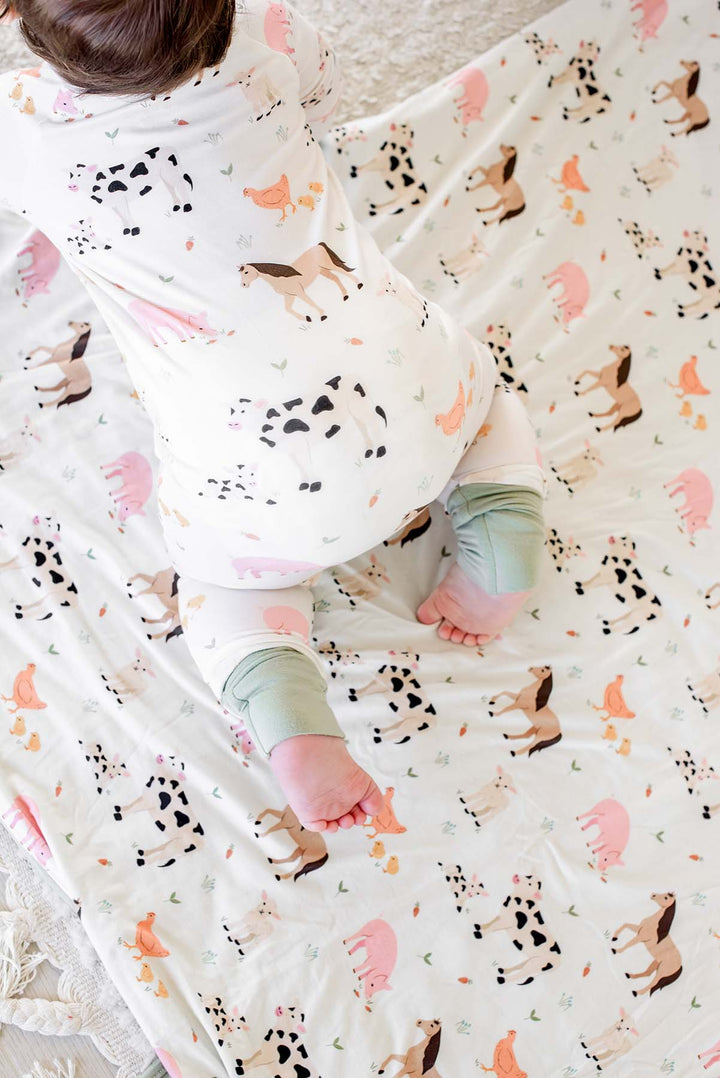 Overhead view of baby crawling in Caden Lane farm animal footie pajamas on matching farm animal blanket