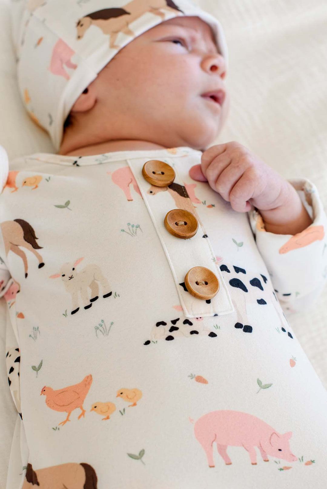 Close-up of Caden Lane farm animal knotted newborn gown showing wooden button placket and matching print topknot hat