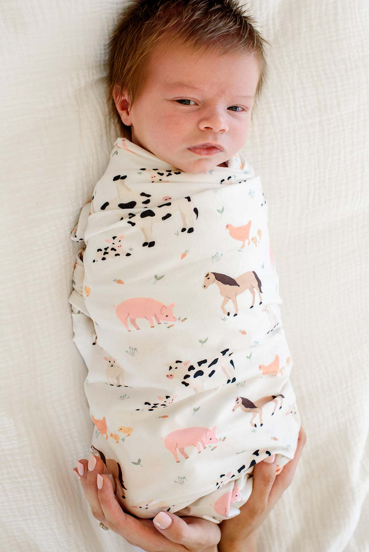 Newborn baby swaddled in Caden Lane farm animal print blanket, held in parent's arms
