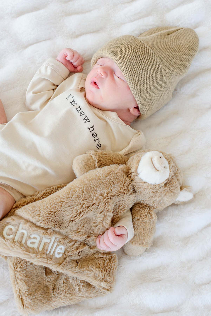 Newborn in a beanie holding a Caden Lane tan horse lovey embroidered with the name "charlie"