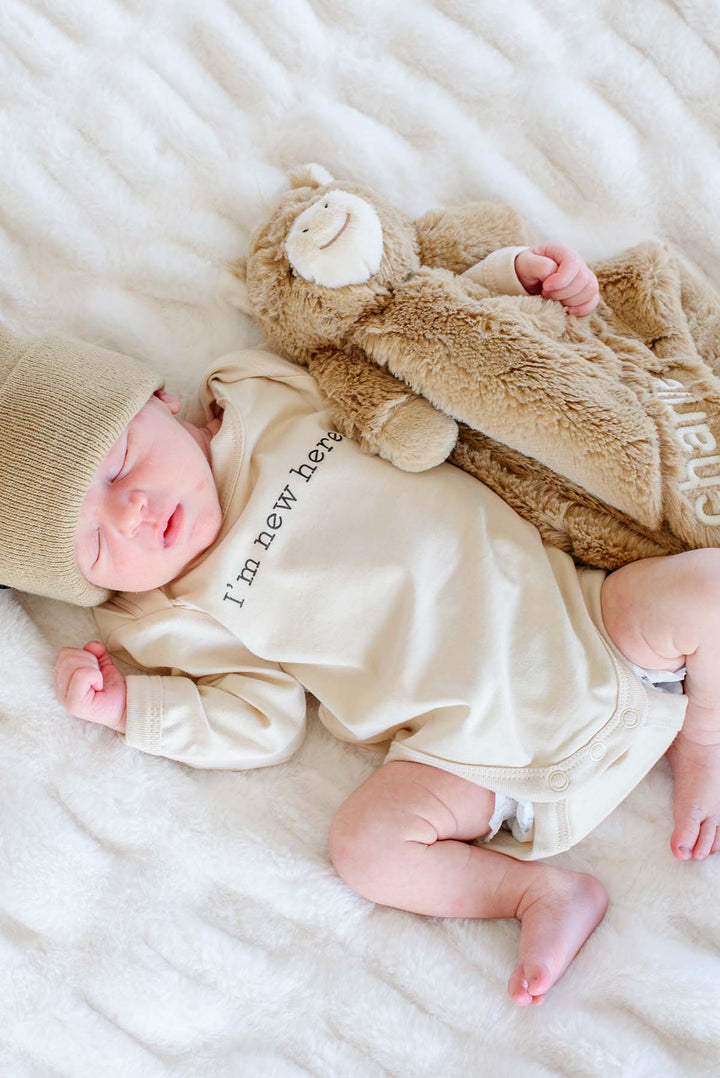 Newborn asleep on a white faux fur blanket next to a personalized Caden Lane horse lovey