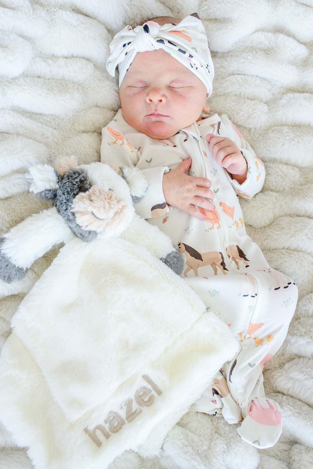 Sleeping newborn beside a Caden Lane cow lovey personalized with "hazel" in taupe embroidery