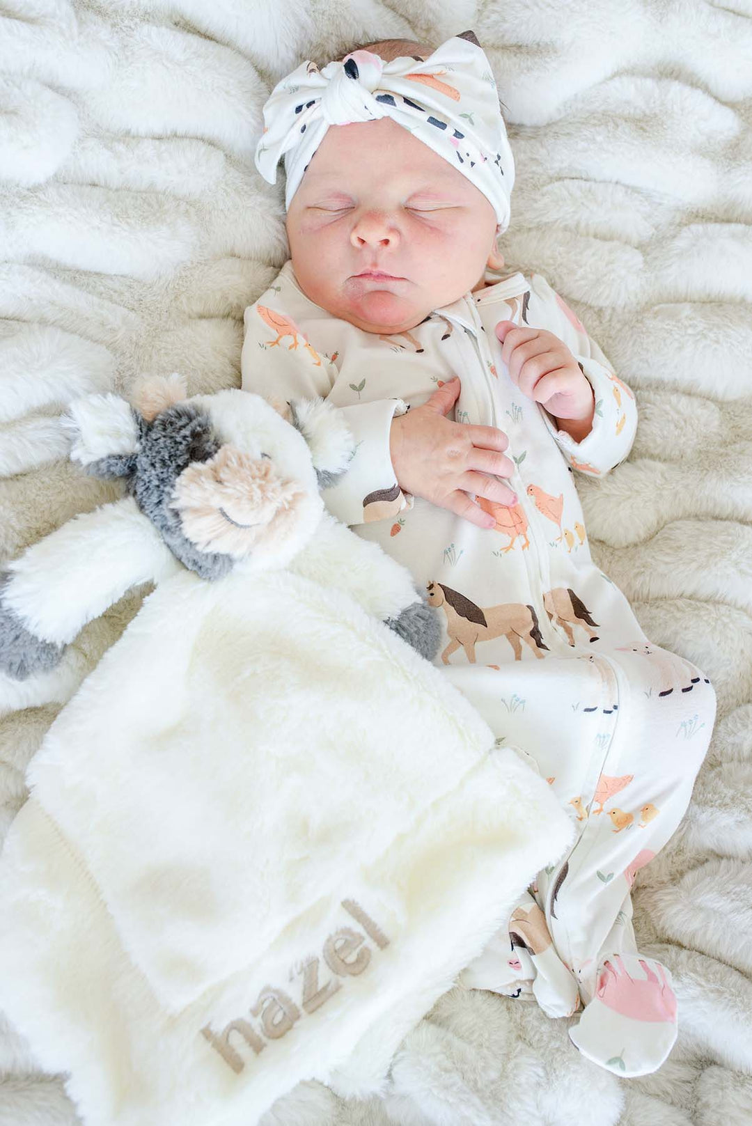 Sleeping newborn beside a Caden Lane cow lovey personalized with "hazel" in taupe embroidery