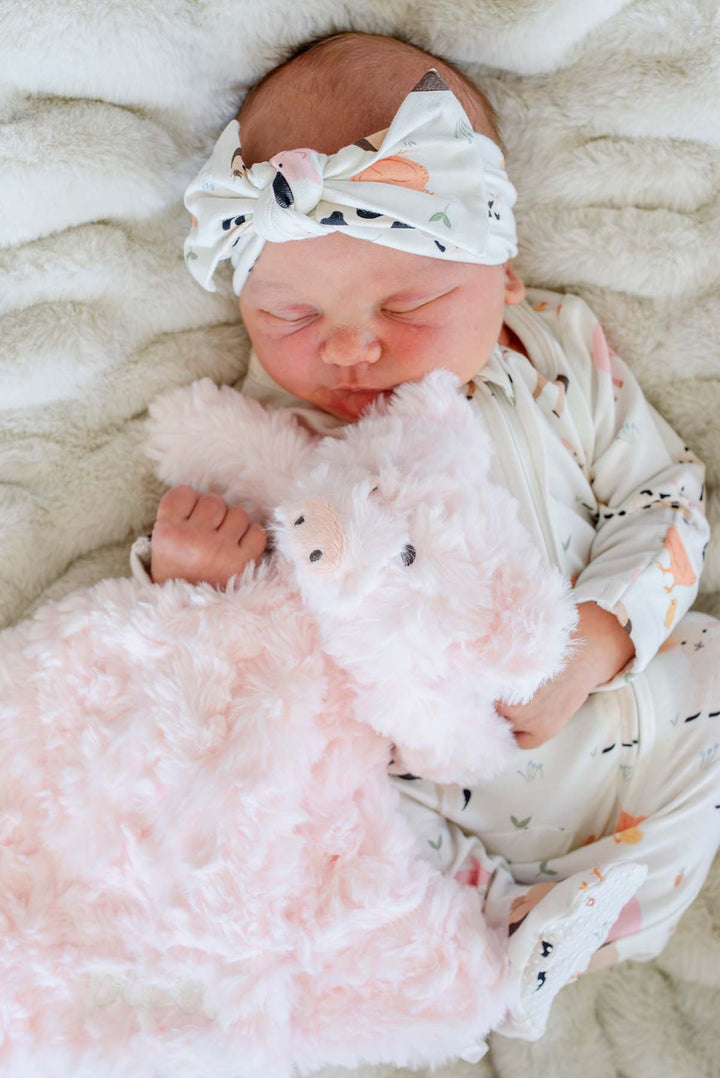 Close-up of a newborn hugging a fluffy pink Caden Lane pig lovey