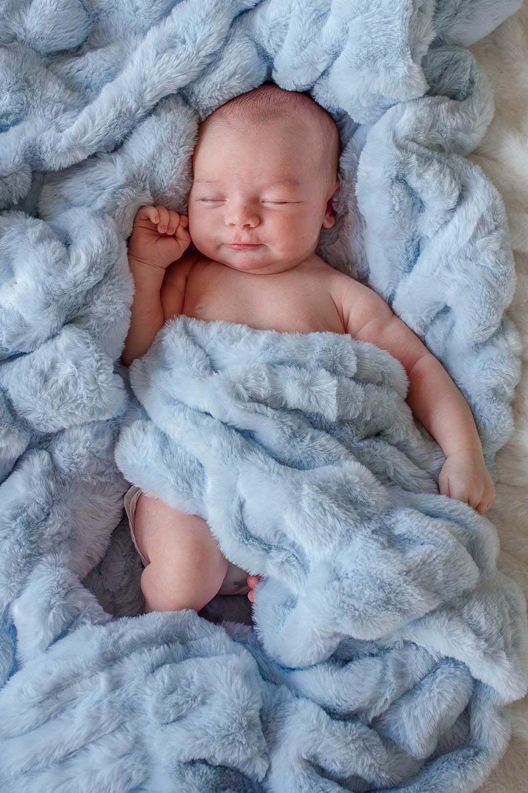 Sleeping newborn baby wrapped in an ice blue double-ruched faux fur blanket