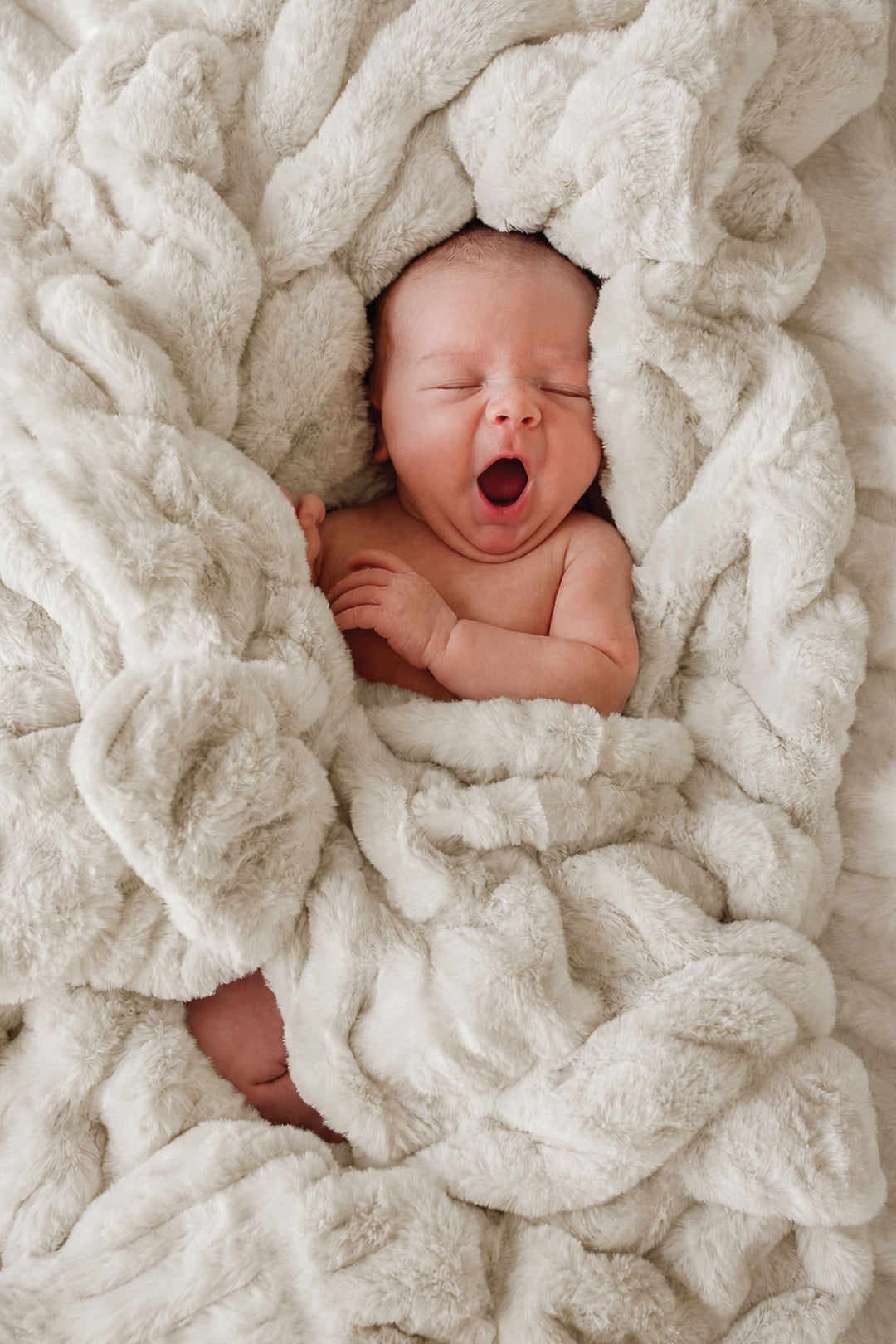 Newborn baby yawning while wrapped in a sand-colored double-ruched faux fur blanket