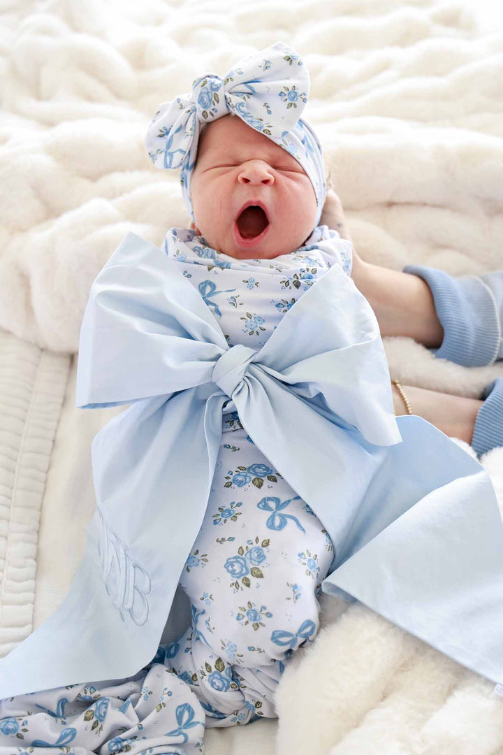 Detail shot of a Tied In Blooms oversized swaddle blanket in blue floral and bow print, tied in a knot