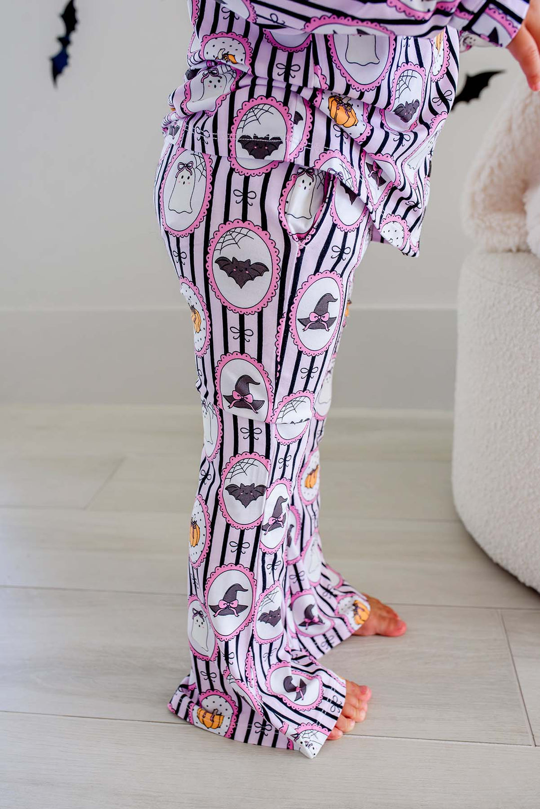Young girl wearing a Caden Lane pink and black striped button-up two-piece flare pajama set with ghost, bat, and pumpkin cameo print