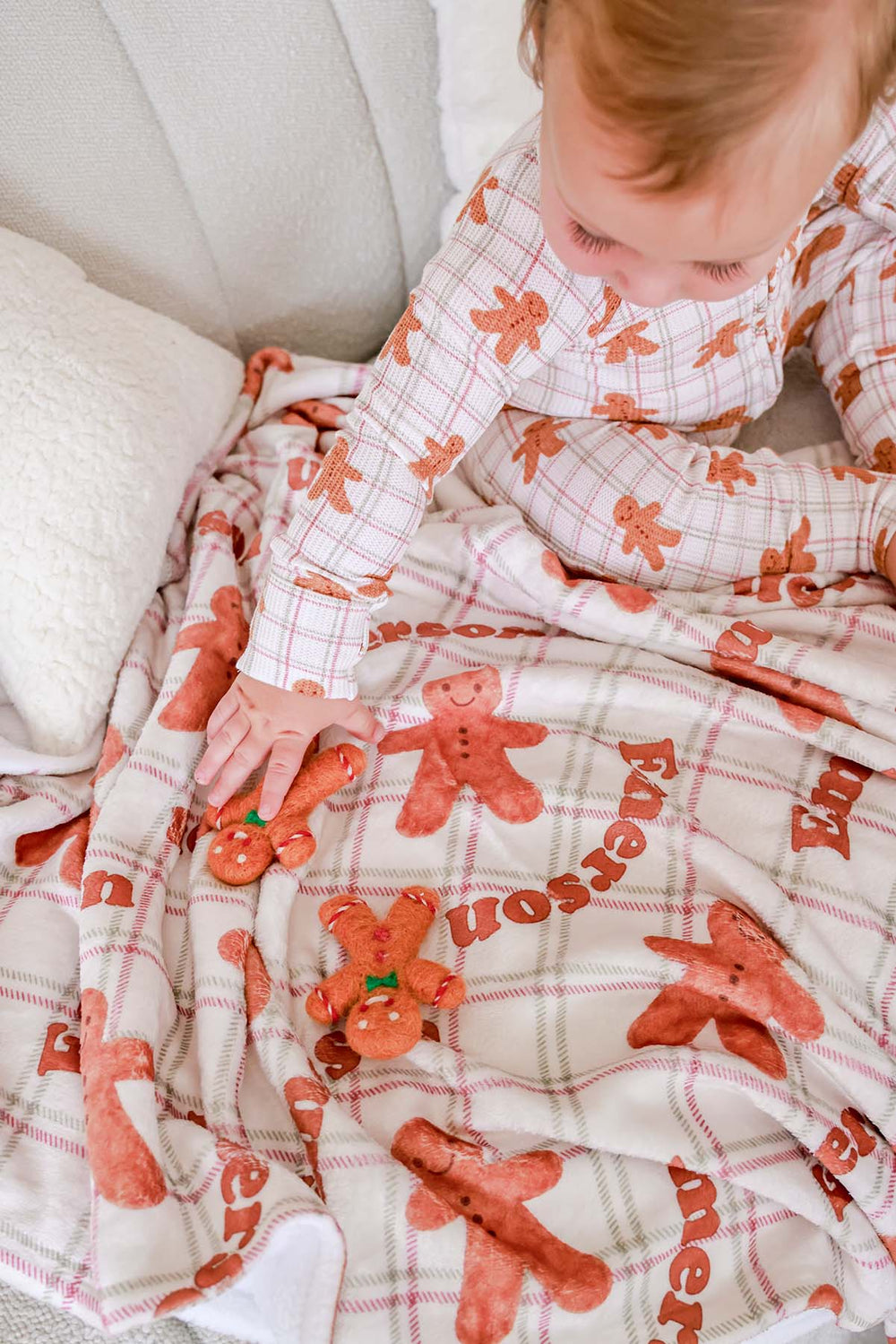 Caden Lane toddler wearing soft bamboo gingerbread cookie print Christmas pajamas while playing with matching gingerbread plush toys on a coordinating holiday blanket, creating a cozy festive scene perfect for Christmas morning, holiday gifting, and family traditions.