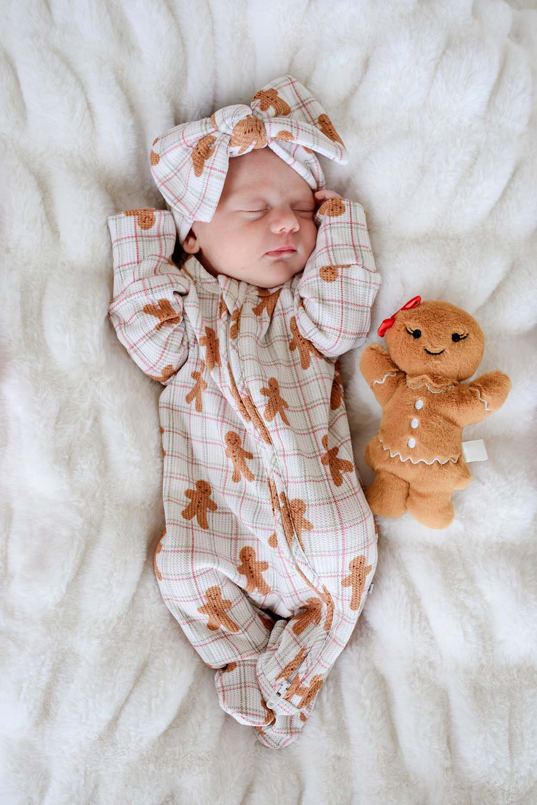 Caden Lane newborn wearing a bamboo convertible zipper romper and matching bow headwrap in a festive gingerbread cookie print, resting beside a gingerbread plush on a cozy blanket—perfect for baby's first Christmas, holiday photos, and winter gifting.
