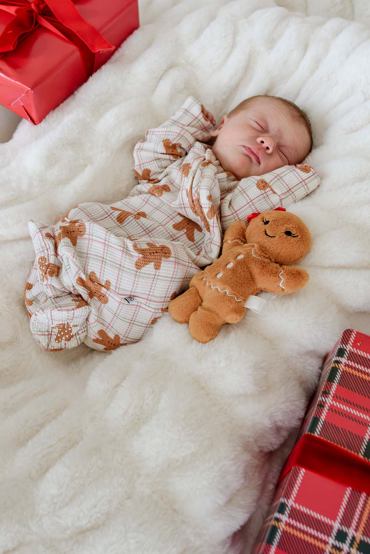 Caden Lane newborn sleeping in a bamboo convertible zipper romper with a festive gingerbread cookie print, resting on a cozy blanket beside a gingerbread plush toy and Christmas gifts—perfect for baby's first Christmas, holiday photos, and seasonal gifting.