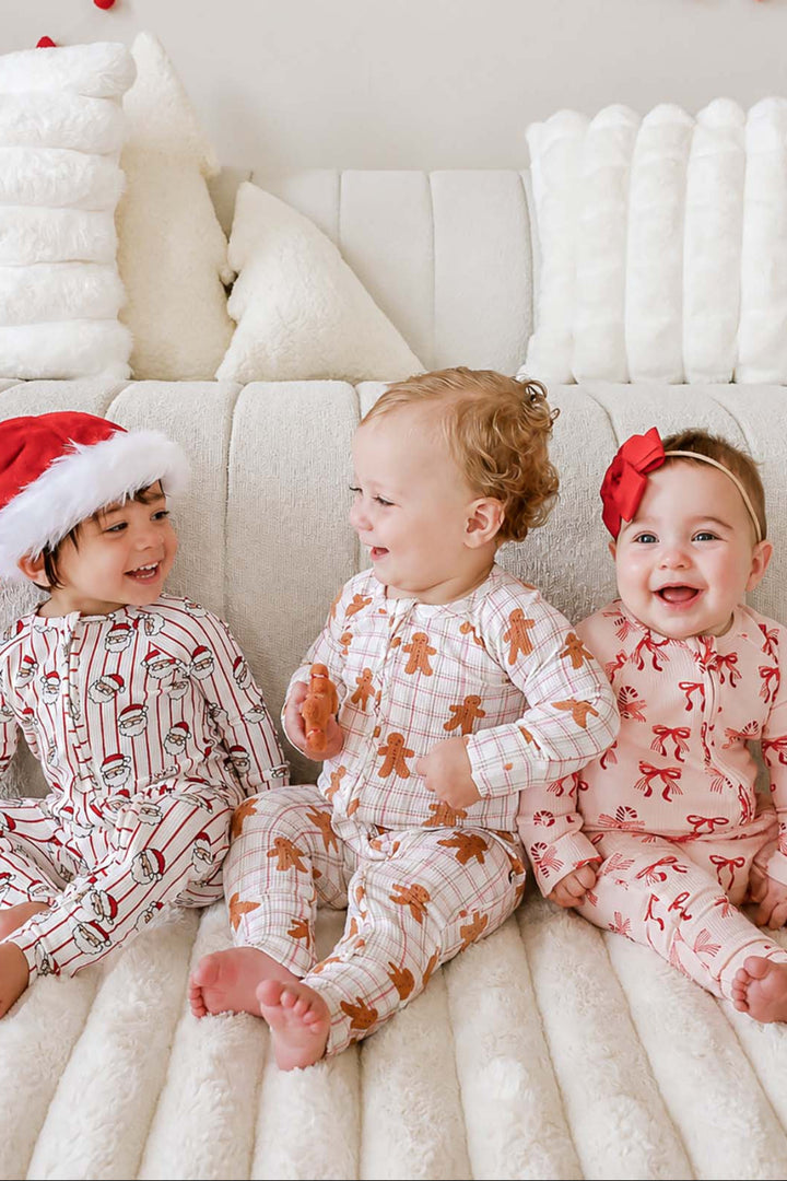 Three babies wearing Caden Lane matching bamboo waffle convertible zipper rompers from the Holly & Jolly, Gingersnap, and Peppermint Bows Christmas collections, sitting together in festive holiday pajamas for sibling Christmas photos.