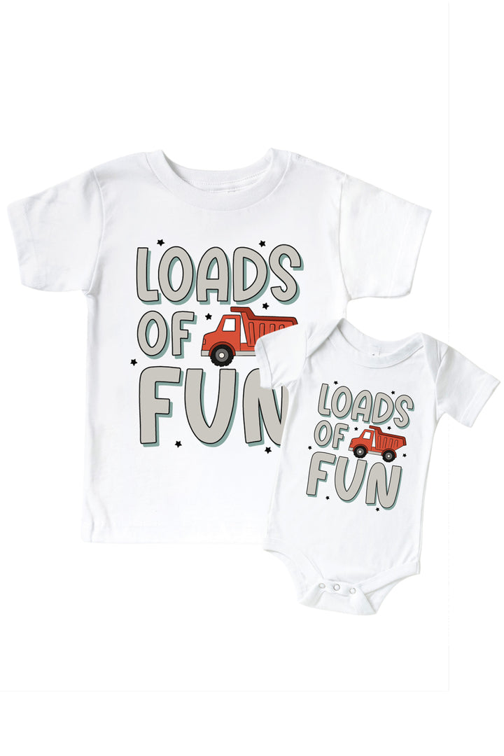 Flat lay of a Caden Lane white tee in a Busy Builder print featuring a red dump truck and black stars, reading "Loads of fun," paired with a matching bodysuit.