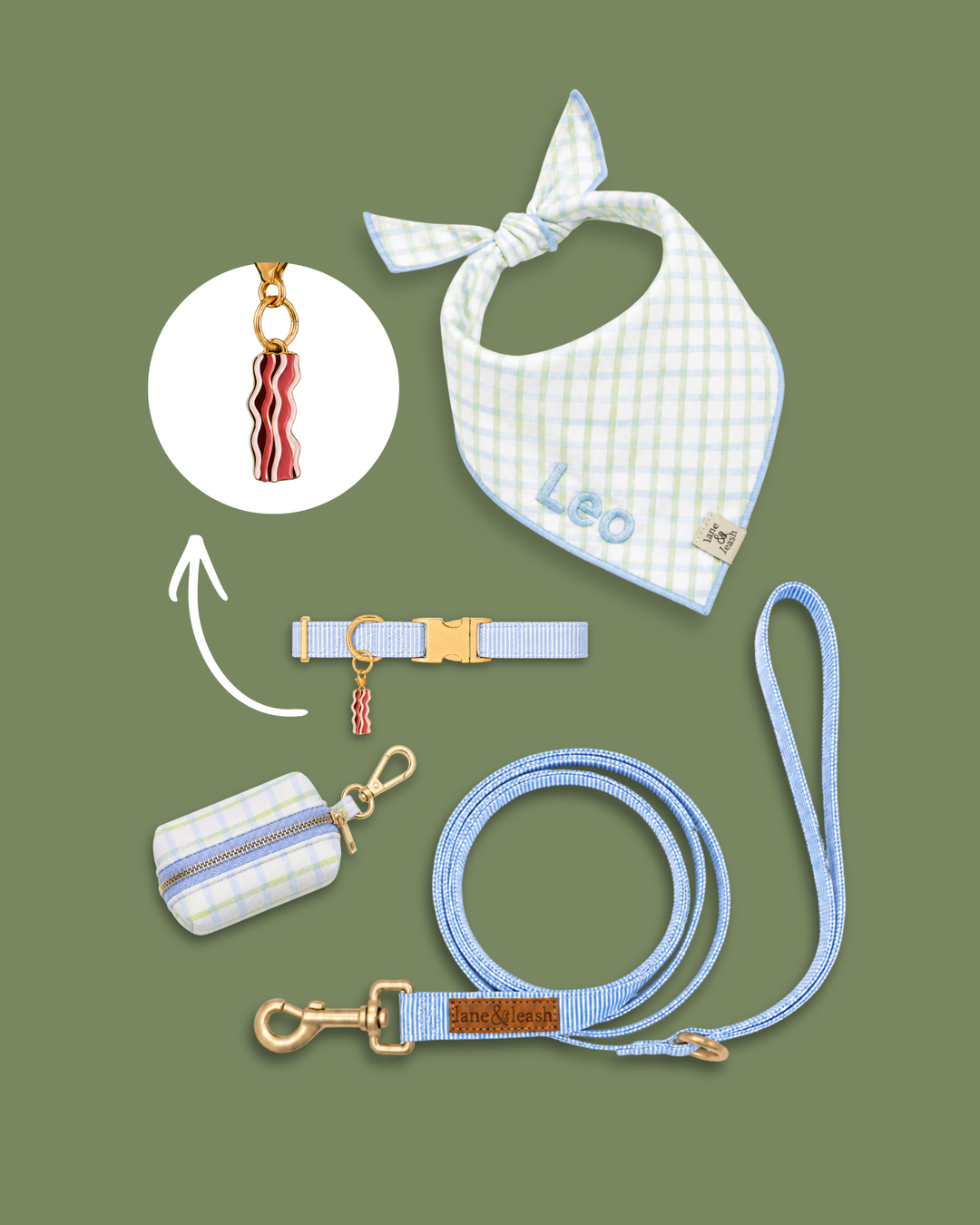 Blue gingham pet accessories flatlay on green background with bandana, collar, leash, and poop bag holder, featuring a bacon strips charm highlighted in a circle callout