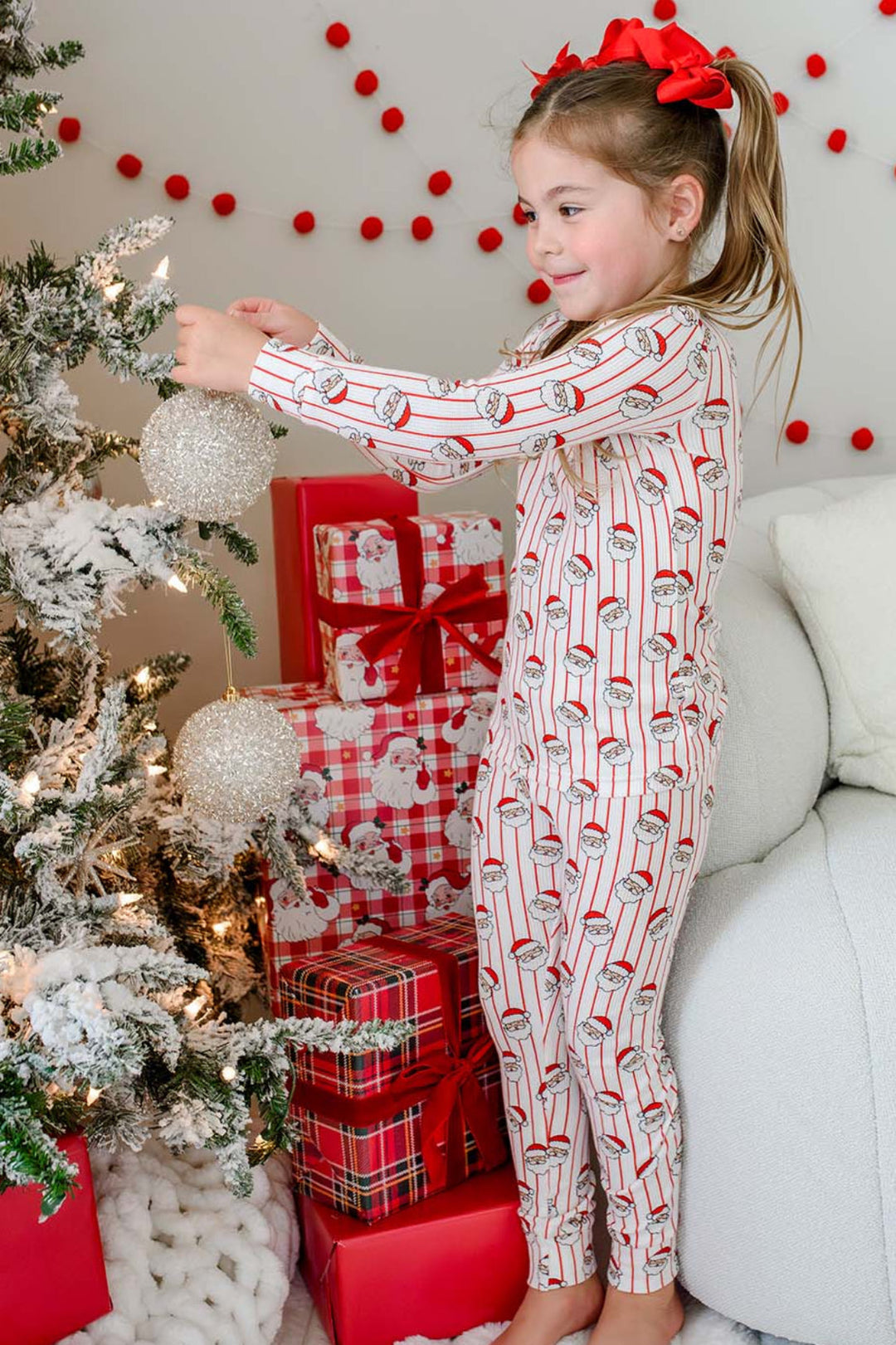 Caden Lane girls' bamboo Christmas pajamas featuring a festive Santa stripe print, shown decorating the Christmas tree in soft, cozy holiday sleepwear for toddlers and kids.