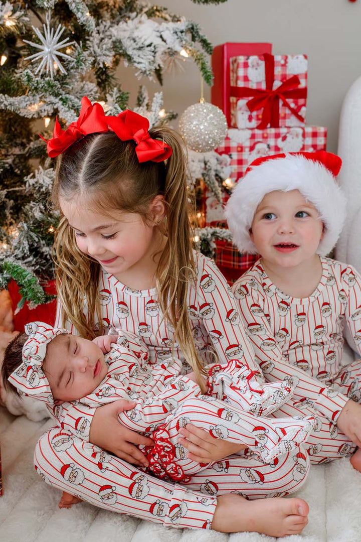Caden Lane matching bamboo Christmas pajamas featuring a festive Santa stripe print, worn by siblings and a newborn in coordinating holiday sleepwear for a cozy Christmas morning by the decorated tree.