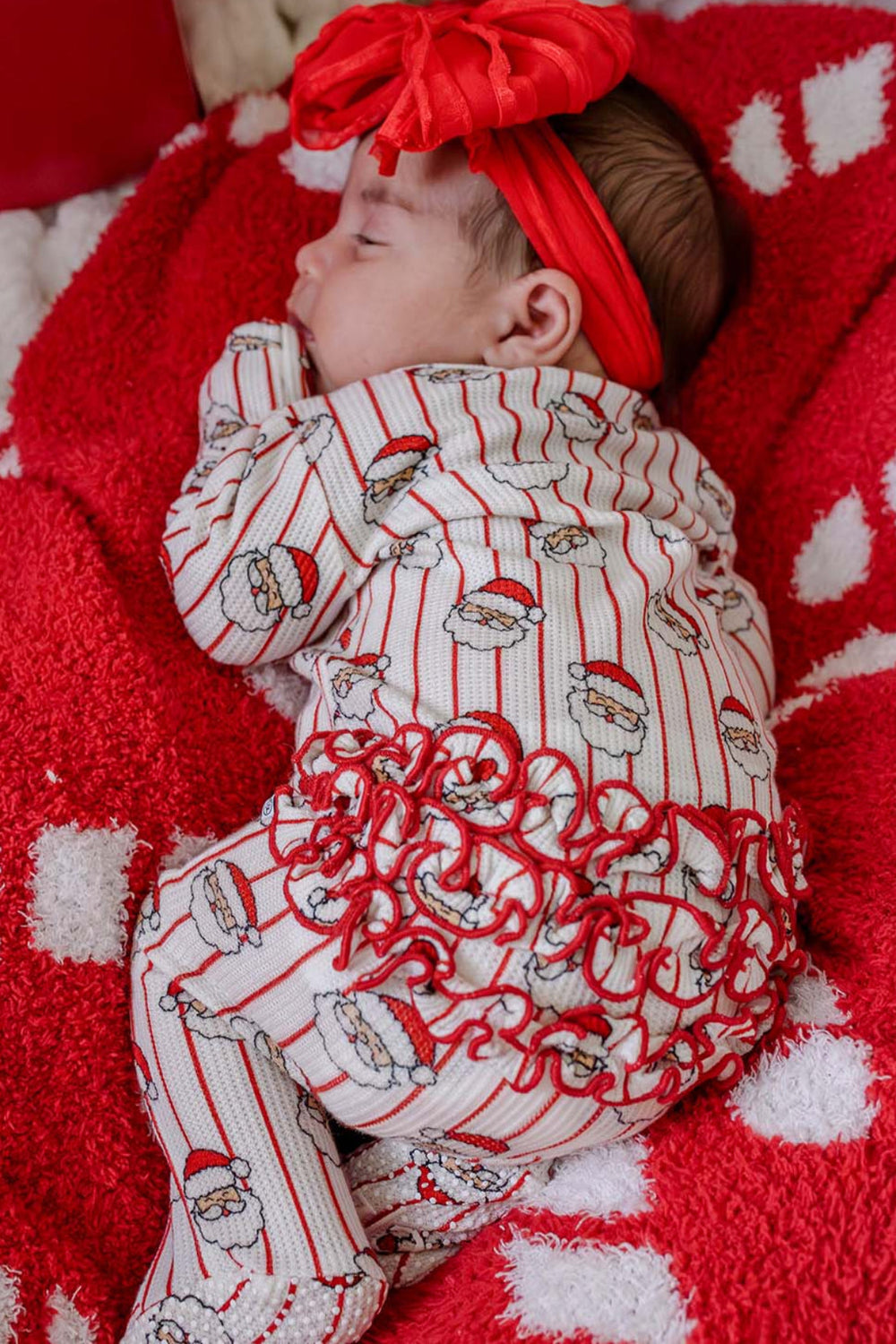 Caden Lane baby girls' bamboo ruffle zipper romper in the festive Santa stripe print, featuring soft bamboo fabric, playful ruffle details, and a matching red bow headband for baby's first Christmas.