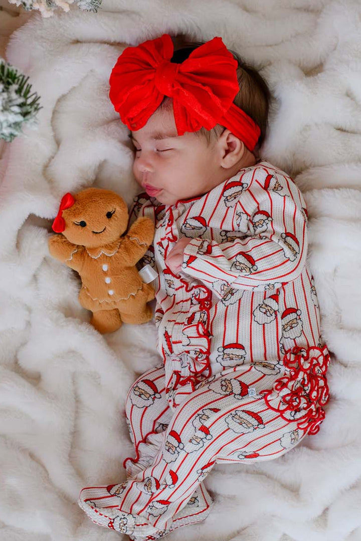 Caden Lane newborn bamboo ruffle zipper romper featuring a festive Santa stripe print, styled with a red bow headband and gingerbread plush for baby's first Christmas and cozy holiday photos.