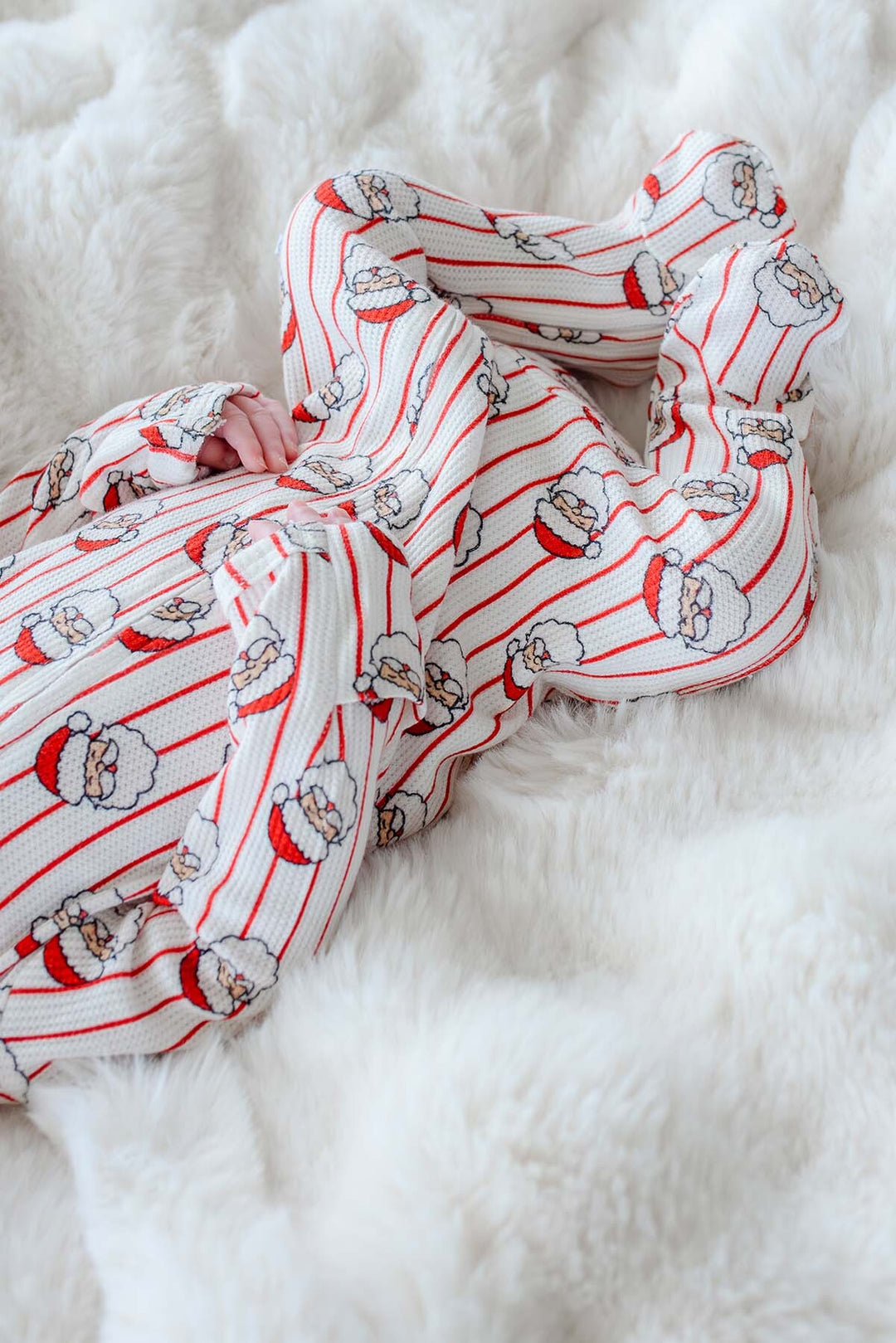 A soft knit scarf with a red and white striped pattern and Santa Claus face prints, draped on a fluffy white faux fur surface.