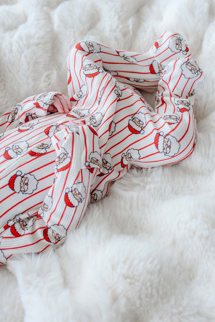 A soft knit scarf with a red and white striped pattern and Santa Claus face prints, draped on a fluffy white faux fur surface.