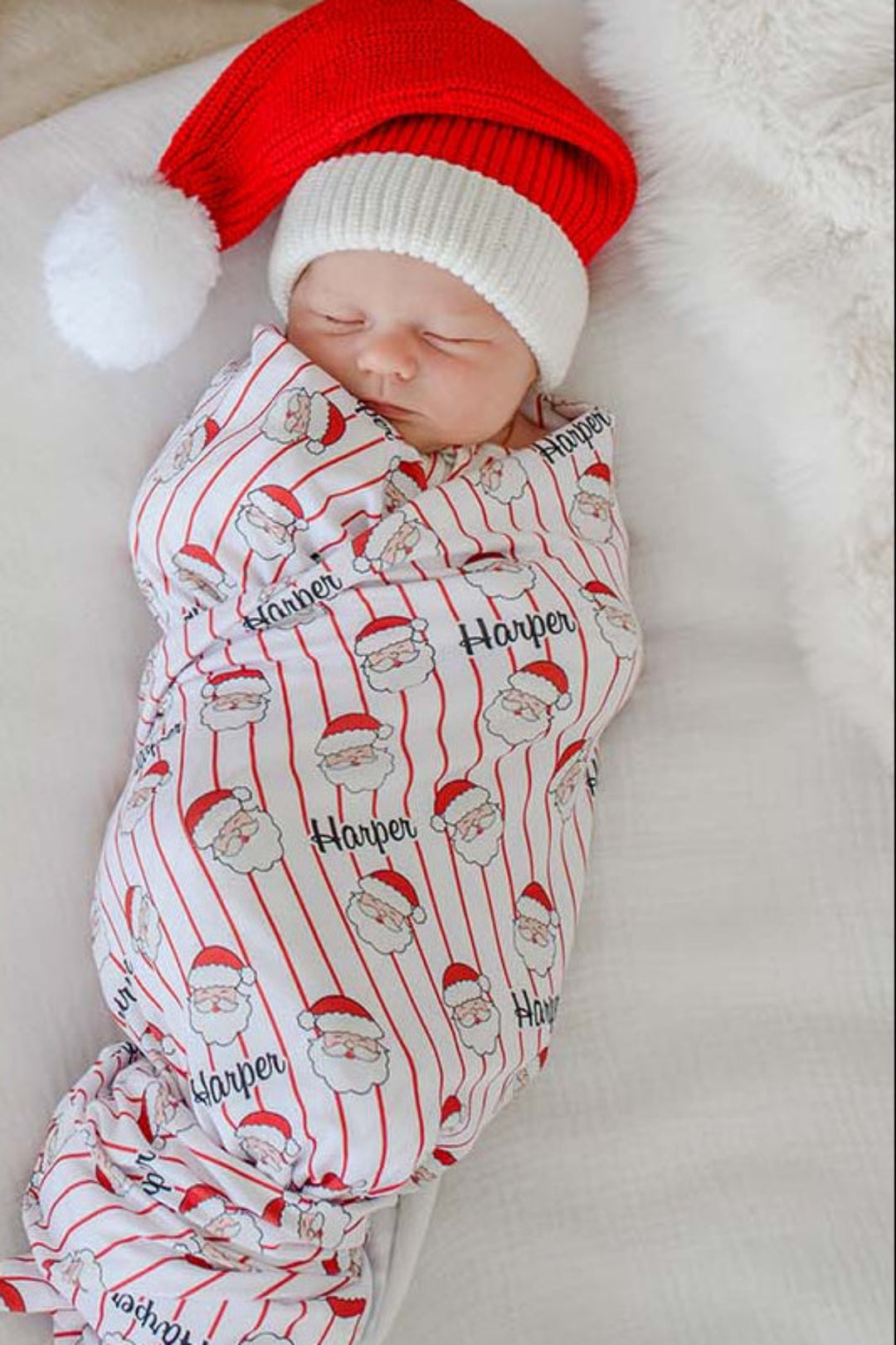 Sleeping newborn wrapped in a personalized Holly & Jolly bamboo swaddle blanket featuring a Santa print on red pinstripes, perfect for Christmas newborn photos and personalized holiday gifts.