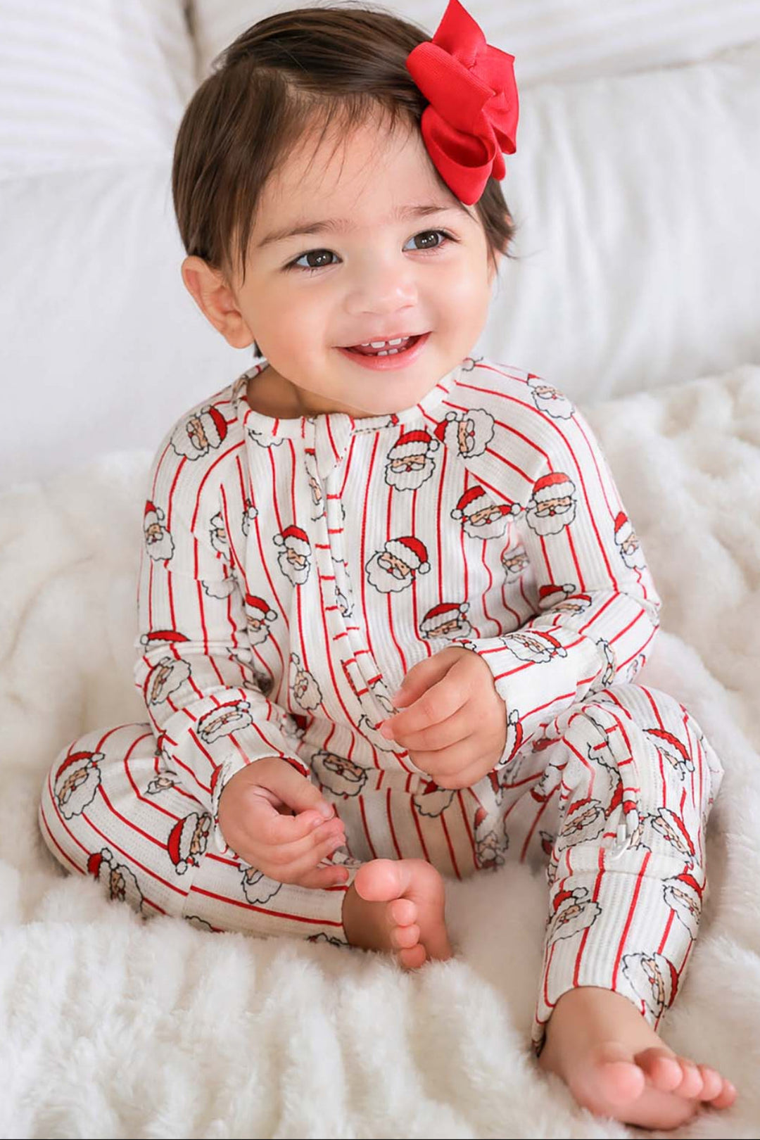 Toddler wearing a Holly & Jolly Christmas bamboo zipper romper featuring a festive Santa print on red pinstripes, perfect for matching sibling pajamas and holiday family photos.