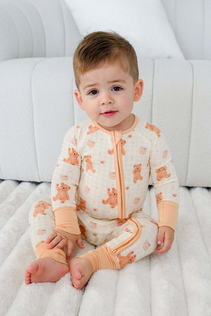 Toddler sitting and wearing a Caden Lane honey bear print convertible romper
