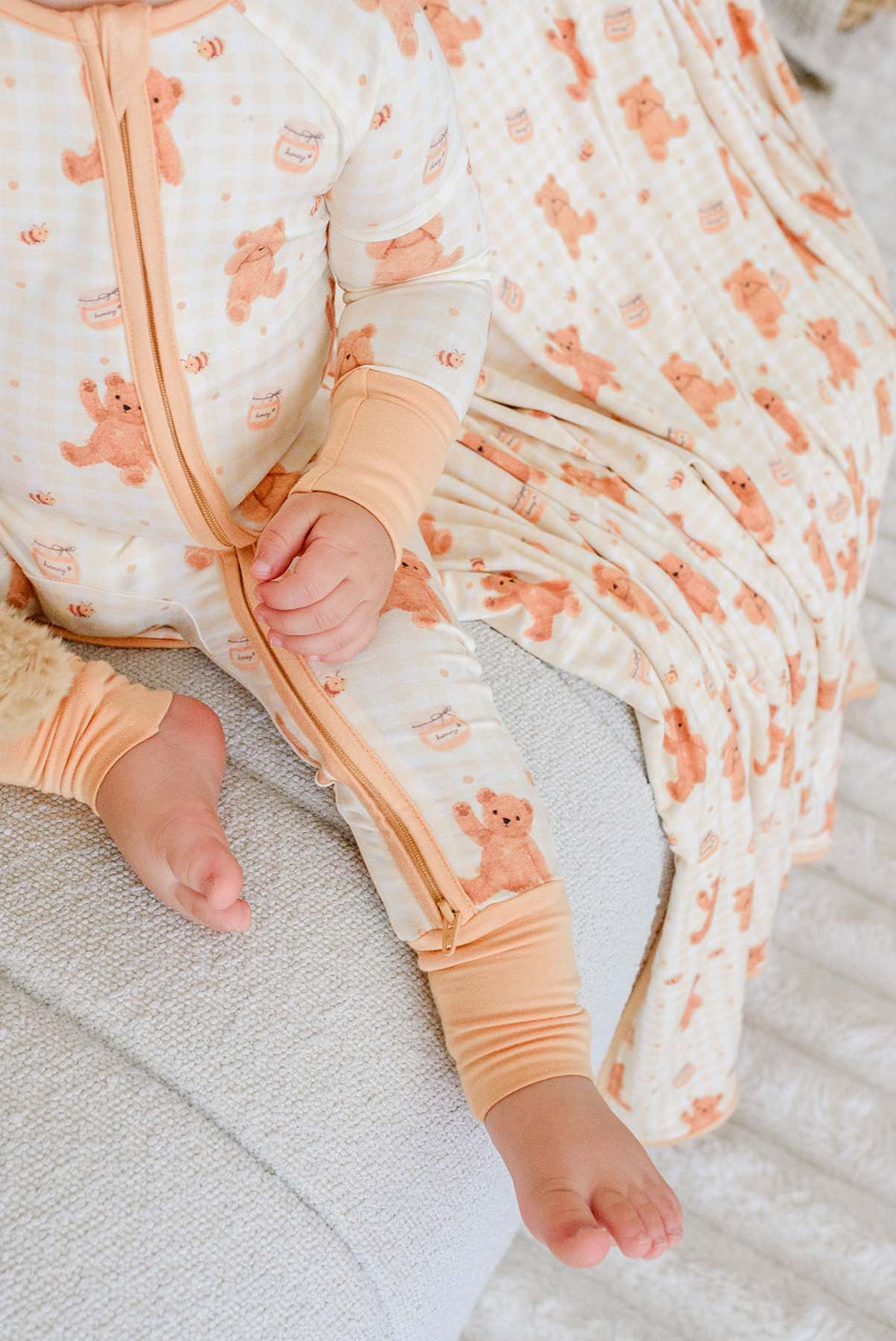 Toddler wearing Caden Lane honey bear print rompers with peach cuffs, sitting on a couch with a matching blanket