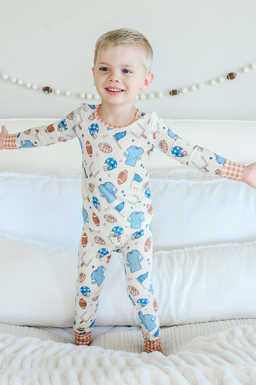 Little boy standing on a bed and wearing the Caden Lane blue huddles and cuddles two piece pajama set.