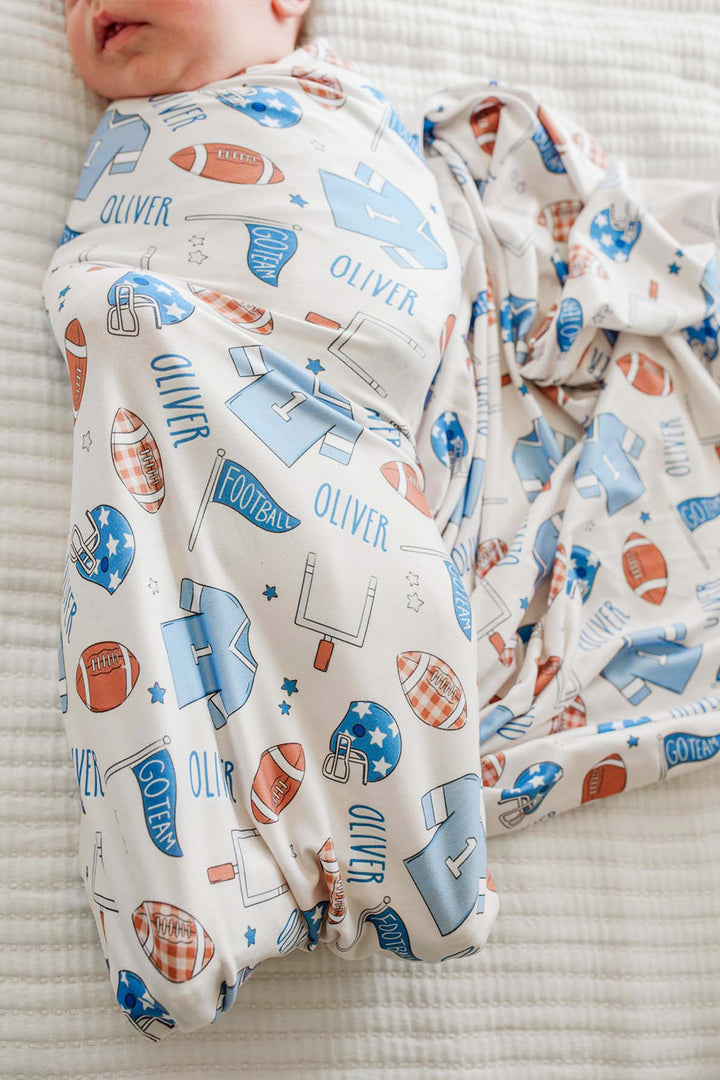 baby wrapped in a Caden Lane huddles and cuddles blue football swaddle. 