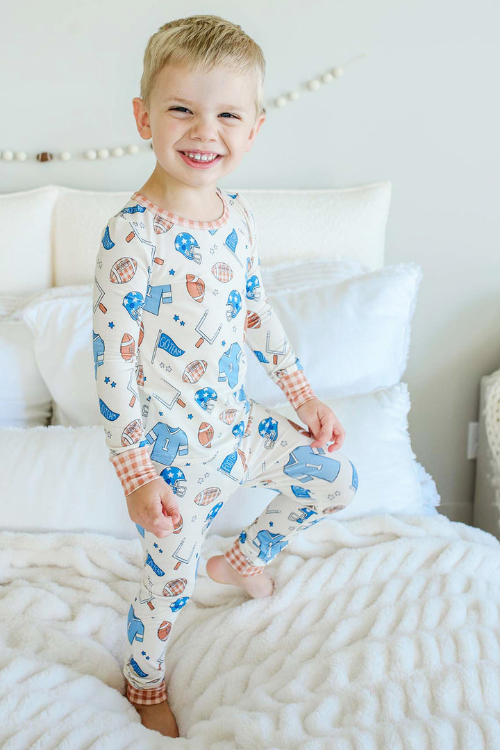Little boy jumping on a bed and wearing the Caden Lane blue huddles and cuddles two piece pajama set.