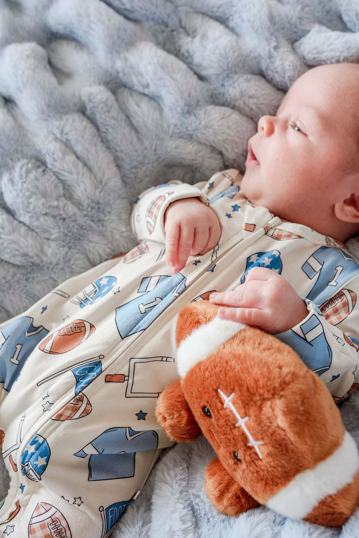 Close up of newborn baby wearing the Caden Lane huddles & cuddles blue zip romper. The print features football prints! 