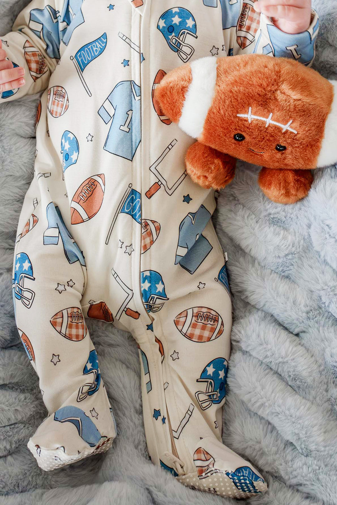 Close up of newborn baby wearing the Caden Lane huddles & cuddles blue zip romper. The print features football prints! 