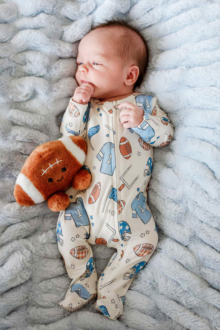 Newborn baby wearing the Caden Lane huddles & cuddles blue zip romper. The print features football prints! 