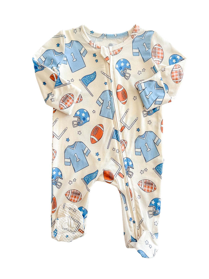 A baby footed sleeper with an all-over sports-themed print on a cream background. The pattern features light blue jerseys, red and orange footballs, blue helmets, and small stars.