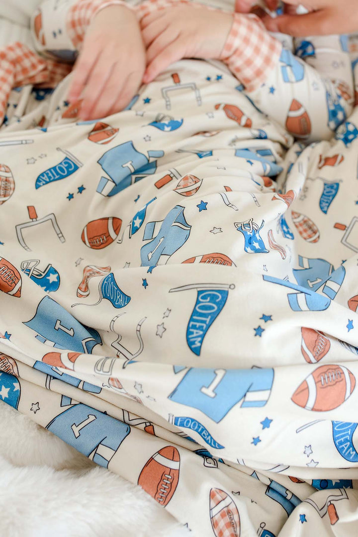 Zoomed in Caden Lane 'Huddles and Cuddles' blue football-print bamboo blanket with orange gingham trim