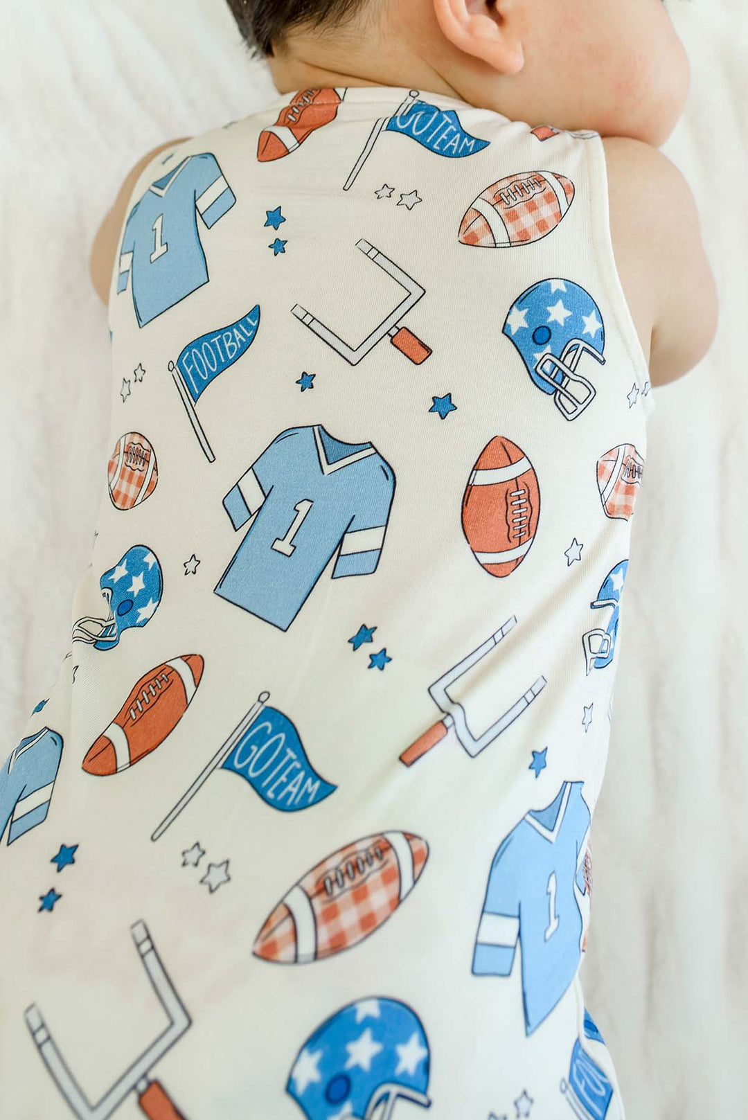 Zoomed in photo of baby wearing a Caden Lane 'Huddles and Cuddles' blue football-print sleeveless romper