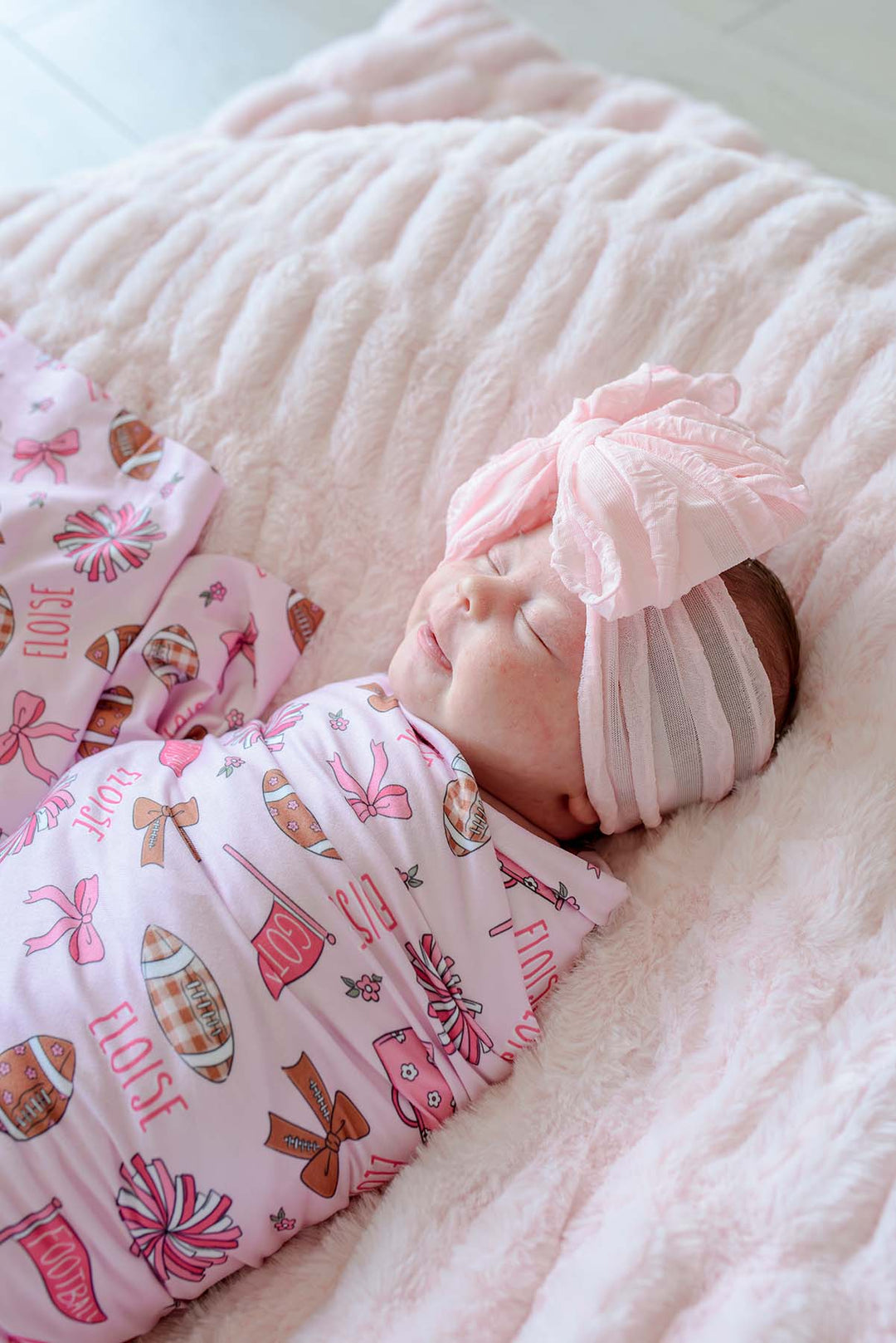 Close up of newborn sleeping in Caden Lane pink football swaddle