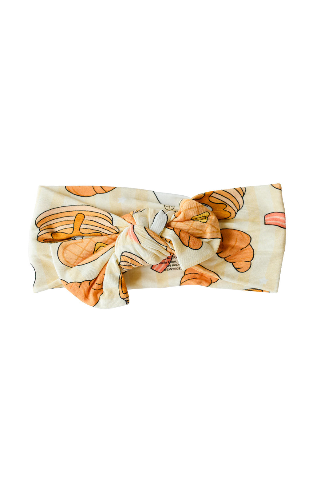 A Caden Lane fabric headband with a knotted bow, featuring an orange and brown pastry pattern on a cream-colored background.