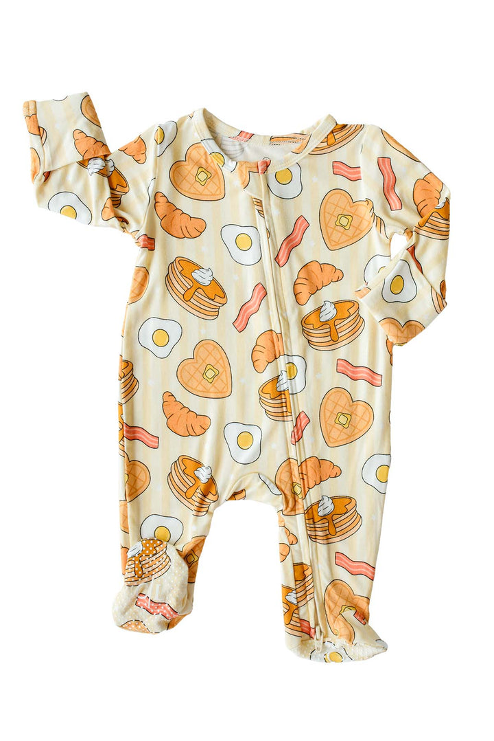 Flat lay of Caden Lane's "I Love You Brunch" print zip-up pajamas, featuring waffles, eggs, bacon, and croissants.