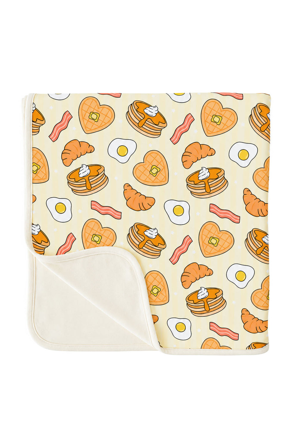 A folded blanket with a breakfast-themed print featuring pancakes, croissants, bacon, eggs, and heart-shaped pancakes on a cream background, with a solid cream reverse side.