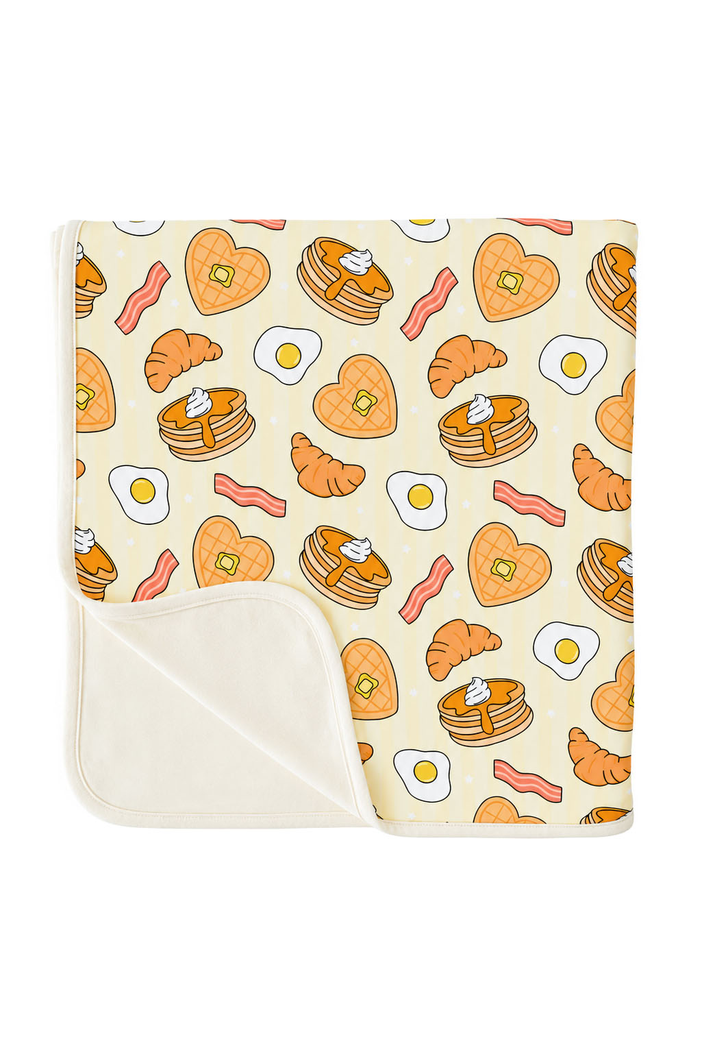 A folded blanket with a breakfast-themed print featuring pancakes, croissants, bacon, eggs, and heart-shaped pancakes on a cream background, with a solid cream reverse side.